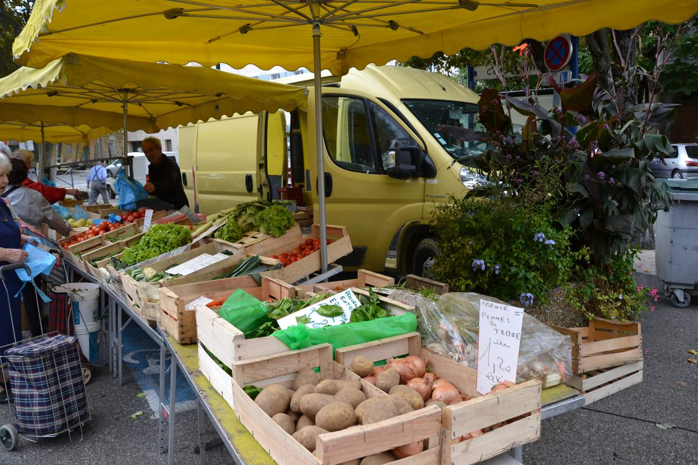 Un étal de fruits et légumes en cagettes sous des parasols jaunes, au marché de Valréas