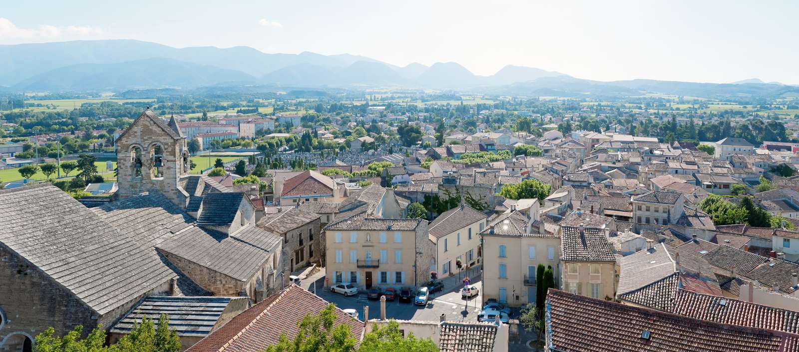 Les toits de Valréas vus d'en haut, la plaine cultivée et les reliefs au fond